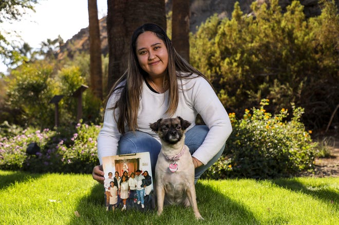 Liz Hernandez poses with a photo of her family from Christmas 2019 and her brother’s dog, Luna, at Bloch Cancer Survivors Park, Wednesday, Dec. 1, 2021, in Rancho Mirage. Liz is caring for her brother Luis’ 3-year-old Chihuahua mix while he is incarcerated. Luis is charged with attempting to kill his mother during a mental health breakdown.