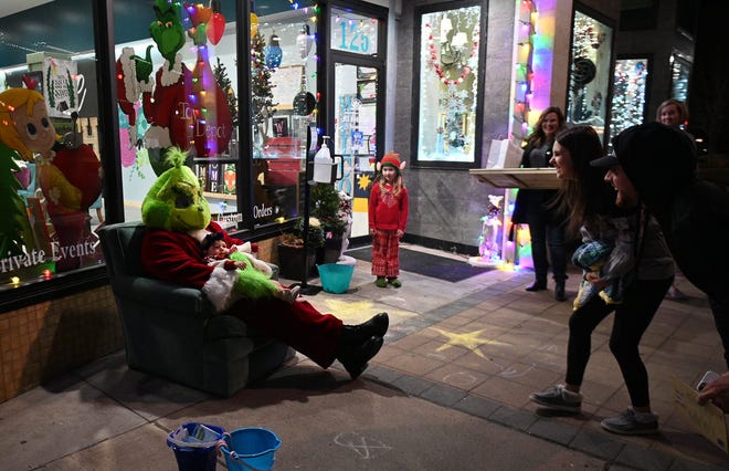 Remi Nava, eight months, sits in the Grinch's lap outside of Splinters-N-Rust while parents Allison and Mario Nava encourage the young girl to smile for photos during the Christmas-themed Third Thursday on Dec. 16, in downtown Hutchinson.