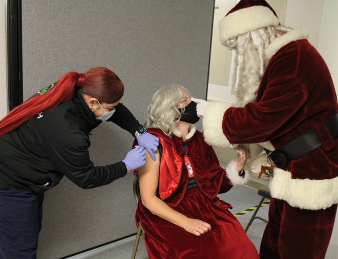 As Elizabeth Lake, a registered medical assistant, administers a COVID-19 booster shot to Mrs. Claus (Michelle Bell), Santa (Dr. Stephen Bell) reassures her. Dr. Bell is a Newport-based internist and primary care physician.