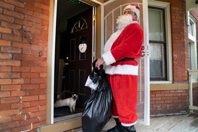 Ray Hillenbrand, 60, of Rochester Hills knocks on the door of Mandy Gutierrez as she gathers her children to be surprised by Santa. The family cat Loco stands by while Hillenbrand waits to hand out toys to the unsuspecting family in Southwest Detroit.