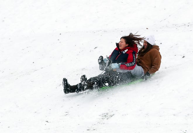 The snow flies as friends Rochelle Dean and Mollie Rose hit the bottom of the hill while sledding at Silver Ridge Elementary School in Silverdale on Tuesday.