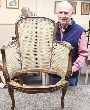 Tom Herron stands with the finished project of a special two-sided, blind-cane chair. In the background two other caners, David Robson (left) and Paul Goard (right), can be seen working on standard hole-cane chairs. Not pictured are Linda Ramsey, also working on a standard hole-cane chair, and Darrell Echelberger, working on a pre-woven cane chair.