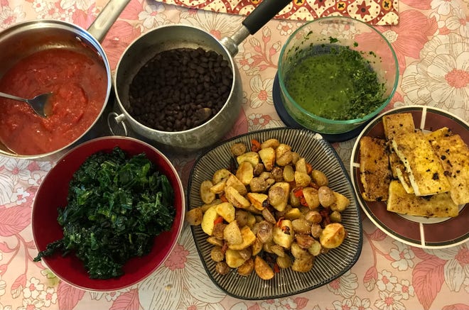 A hearty vegan brunch features pan-seared tofu, pan-roasted potatoes, black beans, kale in olive oil, hearty tomato sauce and green zhug.