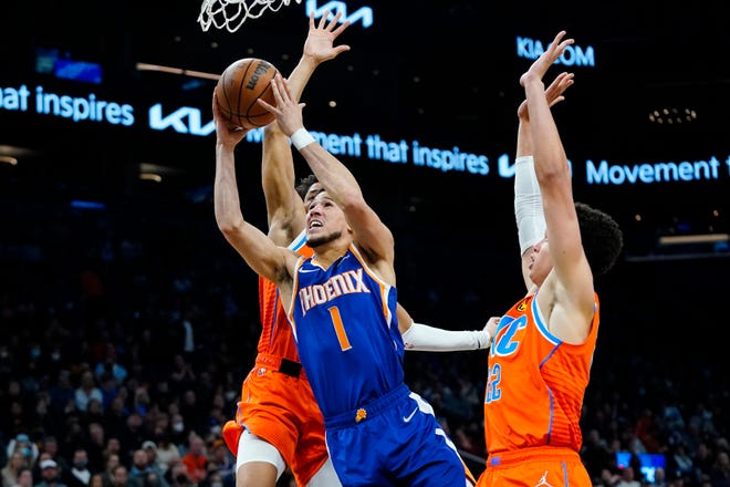 Phoenix Suns guard Devin Booker (1) drives past Oklahoma City Thunder forward Isaiah Roby (22) and guard Aaron Wiggins, left, during the second half of an NBA basketball game Wednesday, Dec. 29, 2021, in Phoenix. The Suns won 115-97.