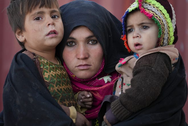 An Afghan woman holds her children while she waits for a consultation outside a temporary clinic in a sprawling building of mudstone huts housing those displaced by war and drought near Herat, Afghanistan, December 16, 2021. The economy of the aid-dependent country tipped already when the Taliban took power in mid-August amid a chaotic withdrawal of US and NATO troops.  The consequences have been devastating for a country plagued by four decades of war, a punishing drought and the coronavirus pandemic.