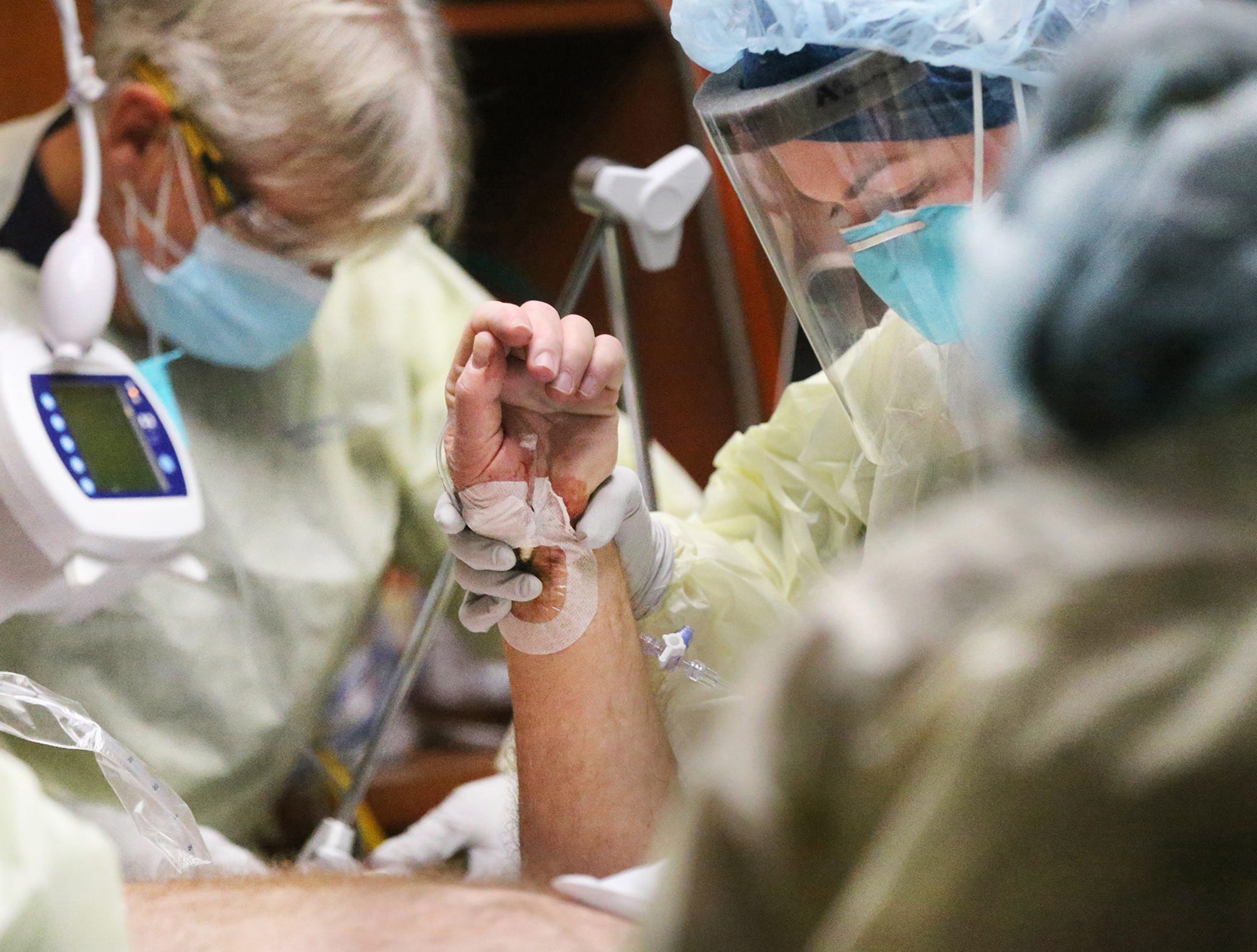 Registered Nurse Becky Roy holds the arm of a COVID-19 patient after Respiratory Therapist Philip Hosmer, left, and a team of nurses and staff flipped the patient to help his breathing.