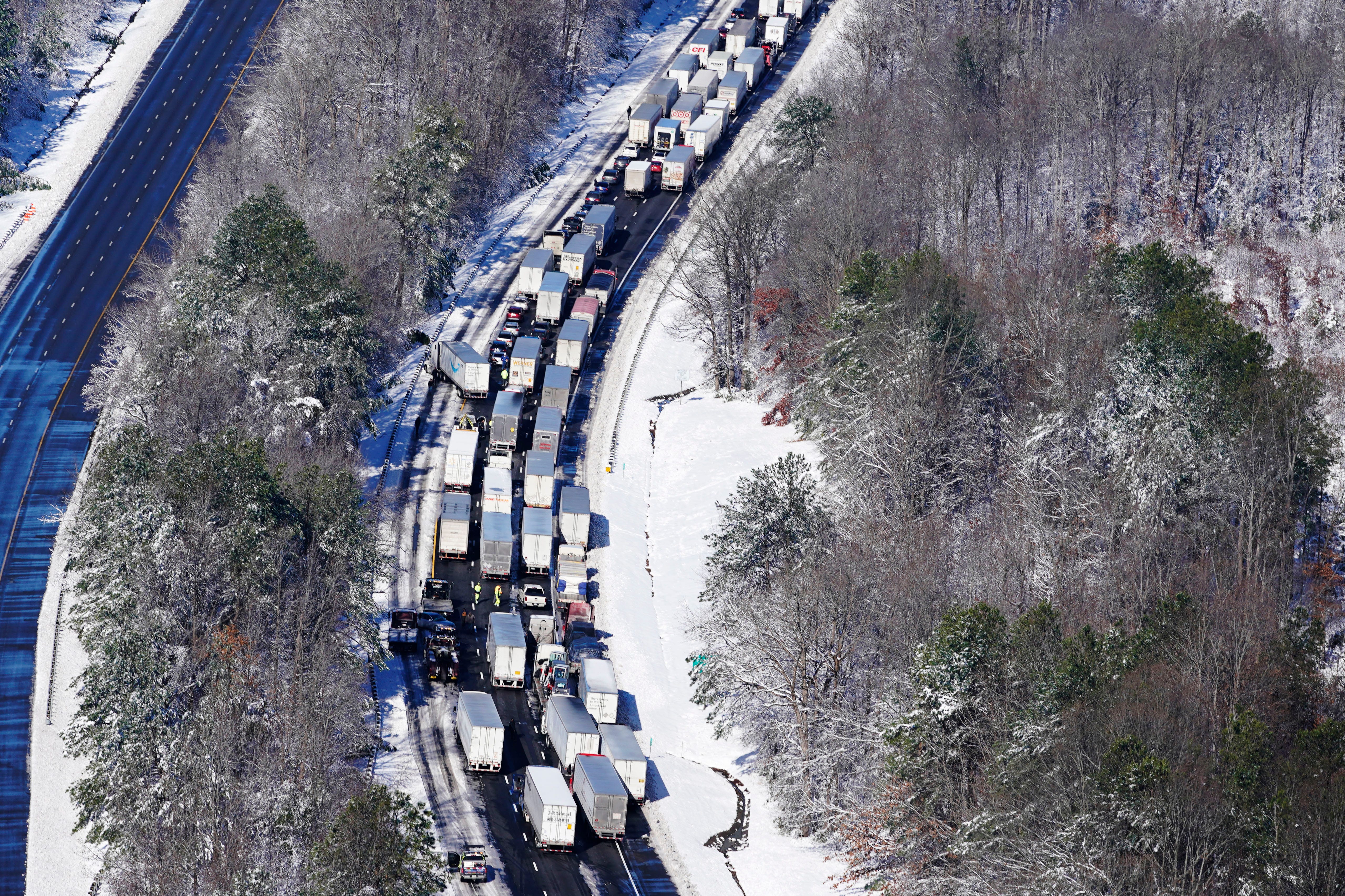 An overhead view of cars in highway traffic with nearby roads blanketed in snow.