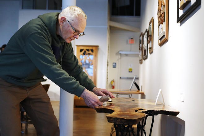 Woodworker and artist Dick Hoisington checks the level of one of his tables on display Friday at the Art Center of Burlington. The Black Walnut Burl tabletop was milled from a tree collected in western Illinois in 2018 and mounted on an antique refurbished Singer treadle base. Hoisington's work is part of the upcoming Earthly Treasures exhibit featuring for by local wood-and-metal artisans.