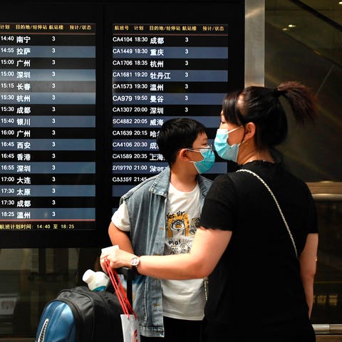 Travelers wearing face masks wait in front of a de