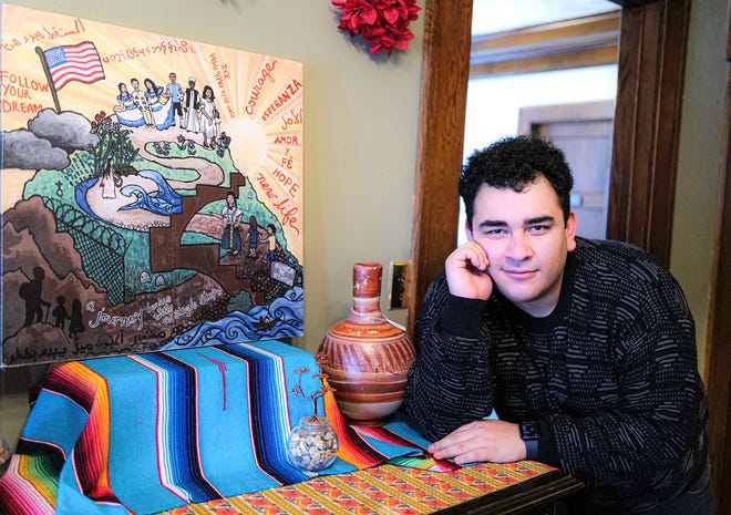 Edwin Rigoberto Hernández-Ventura, a refugee from Honduras, with a painting he and other immigrants created as part of The Samaritas Youth Refugee Art exhibit on display at Casa de Rosado in Lansing Tuesday, Jan. 18, 2022. Edwin, now 22, started his journey to the United States when he was 14 and now has a green card.