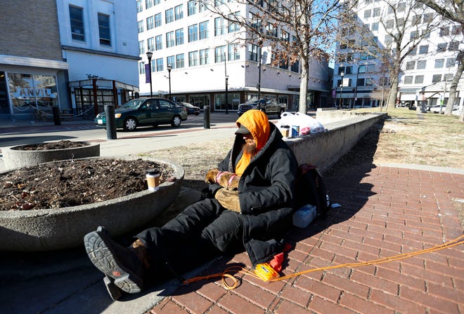 John, who is homeless, attempts to keep warm sitting in the sun with his friends dog, named Felony, on the Park Central Square while his friend charges electronics in the downtown library on Thursday, Jan. 20, 2022.