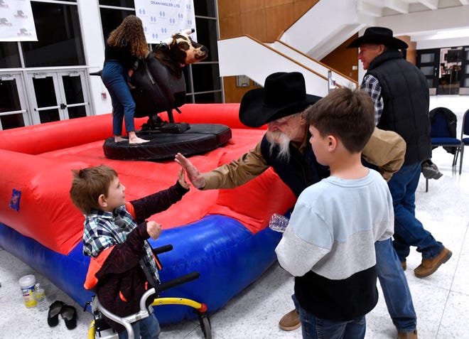 Charles Flournoy, 8, gives Jim Nolan a high-five after riding the mechanical bull in the Rehab's "Olympic Village" in the lobby of the Abilene Convention Center on Saturday. Charles is a client at West Texas Rehabilitation Center, which was holding its 2022 Rehab Telethon and Auction there.