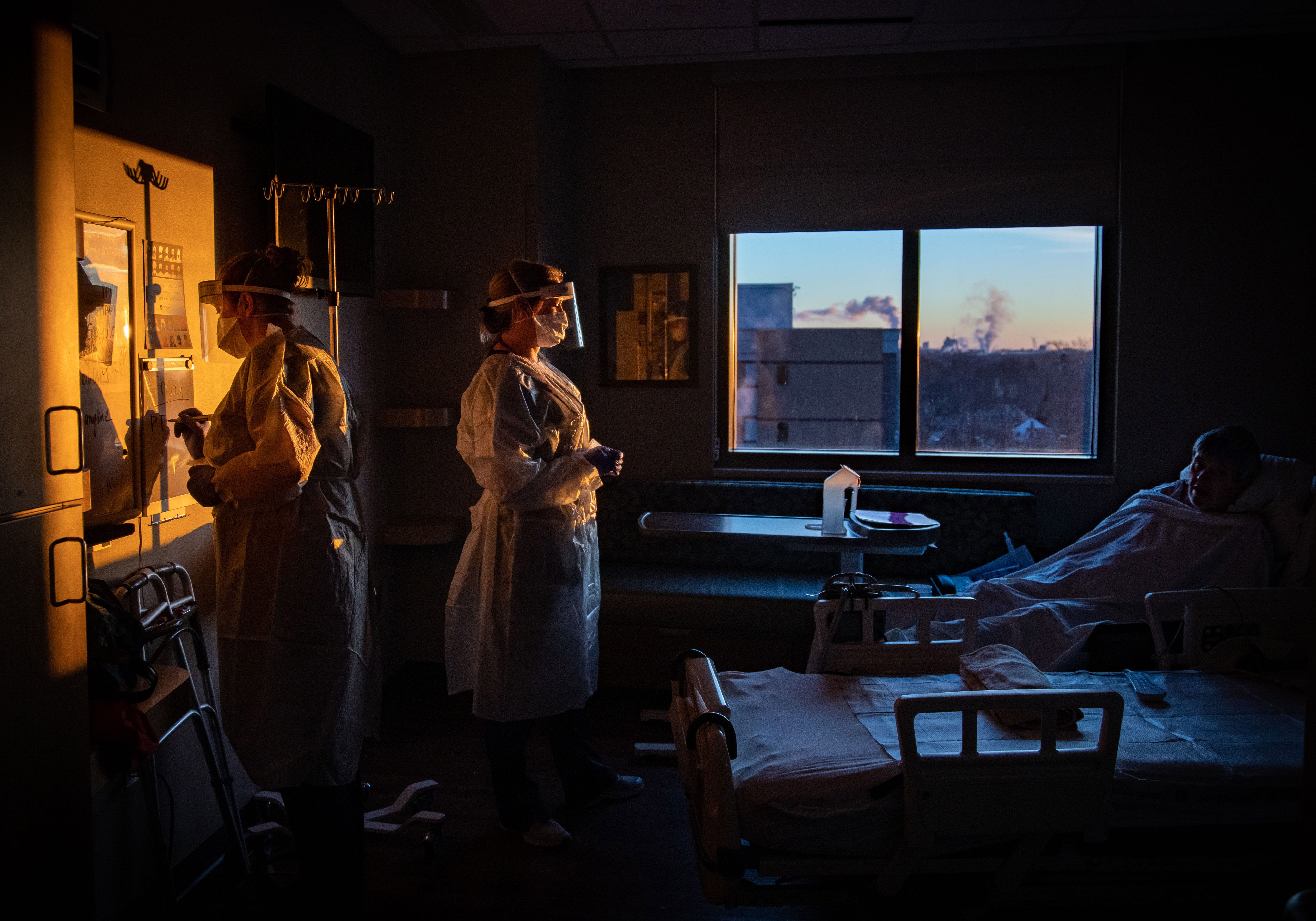 Nurses Emily Owen and Stephenie Simmons wear protective gowns, masks and face shields to check on a COVID-19 patient as the sun rises outside Mary Greeley Medical Center in Ames, Friday, Jan. 7, 2022.