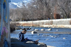 Katherine Ryan writes in her journal while sitting in the sun next to the Truckee River in downtown Reno on Jan. 25, 2022.
