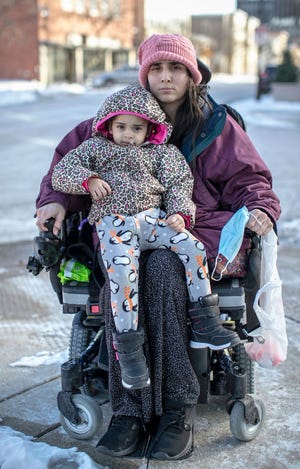 Ashley Lagoo-Mckinnie and her daughter, Lyanna Brown-Lagoo, sit on the corner near the Above and Beyond Children's Museum, Friday, January 28, 2022, in Sheboygan, Wis. Ashley, who uses a wheelchair, and her young daughter live in a shelter in Sheboygan. The shelter has everyone leave in the morning and not return until the late afternoon, no matter what the temperature outside is.