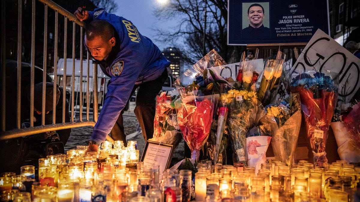 A New York City Police Department officer lights a candle at a makeshift memorial outside the New York Police Department's 32nd Precinct, near the scene of a shooting that claimed the lives of NYPD officers Jason Rivera and Wilbert Mora in the Harlem neighborhood of New York, Monday, Jan. 24, 2022.