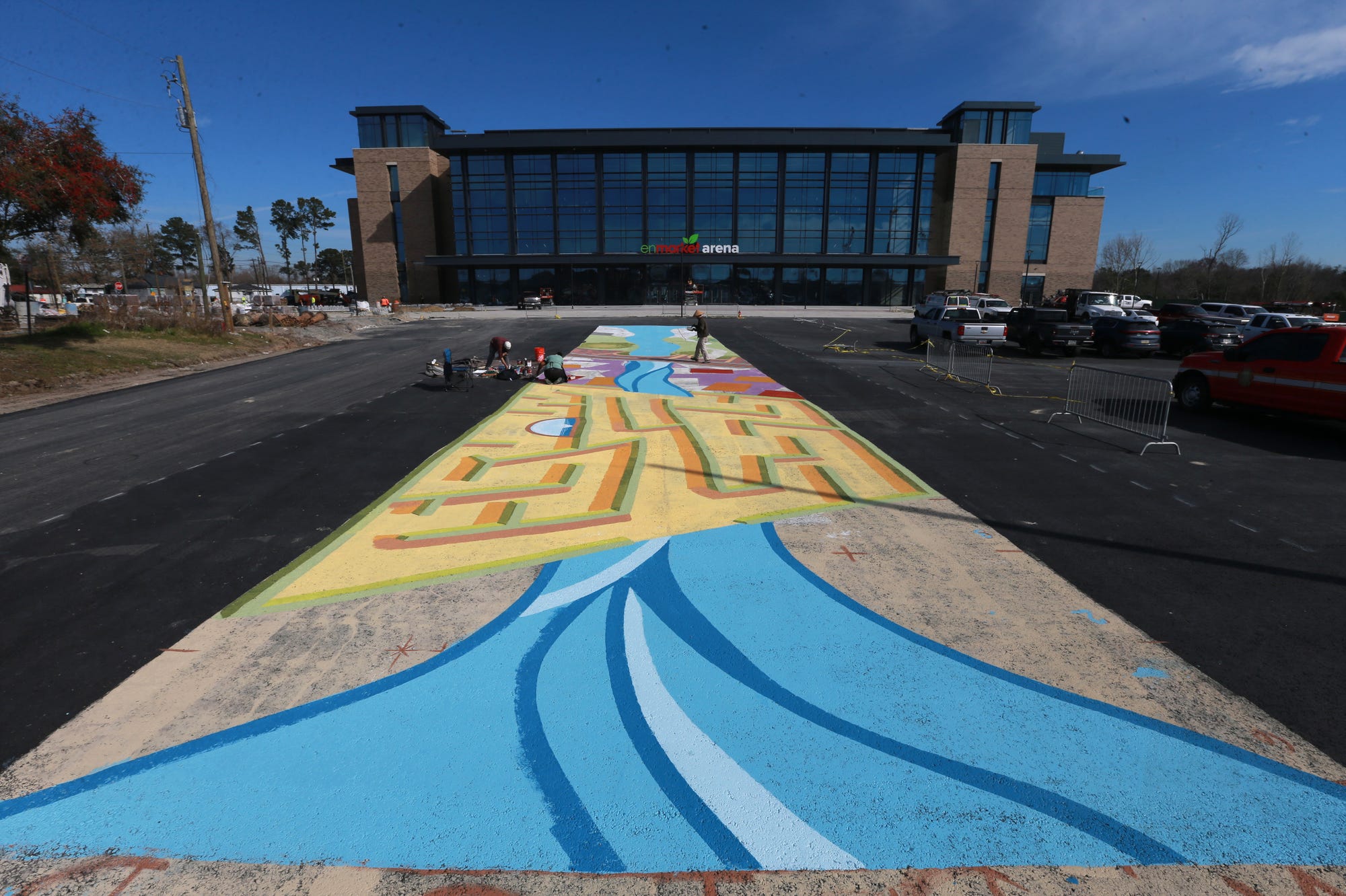 Artists Nae'Keisha Jones, Alfredo Martinez, and Brian MacGregor work on a mural on the ground just outside the new Enmarket Arena. Xavier Hutchins is the fourth artist with the team that designed the mural.