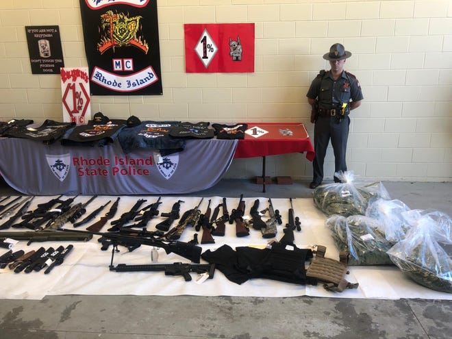 A Rhode Island State Police trooper stands guard over guns and other items seized during a 2018 raid on motorcycle gangs in the state.