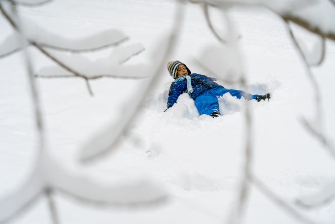 Zander Heyza, of Flint, makes a snow angel in the street as his mother Negan Heyza shovels outside of their home on Thomson Street in Flint on Feb. 2, 2022, after his school was canceled following an early morning snowstorm that blanketed the area.
