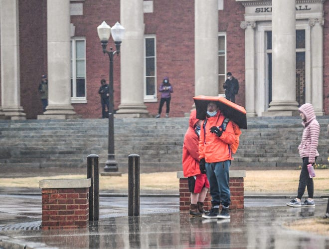 Clemson University students wait on a corner near Sikes Hall Administration, keeping a mask under their chin outdoors, while required to wear the face coverings inside campus buildings in Clemson, S.C. Thursday, February 3, 2022.  Policy also states "except when alone in spaces such as private workspace, classrooms, or housing rooms or when eating or drinking."