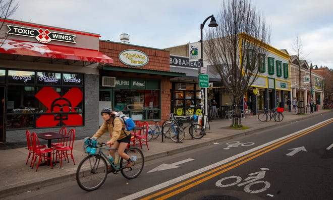A person cycles past the part of the block along East 13th Avenue near the University of Oregon that is scheduled to be developed by The Duck Store into mixed-use commercial and apartment space. Monday, Feb. 7, 2022.