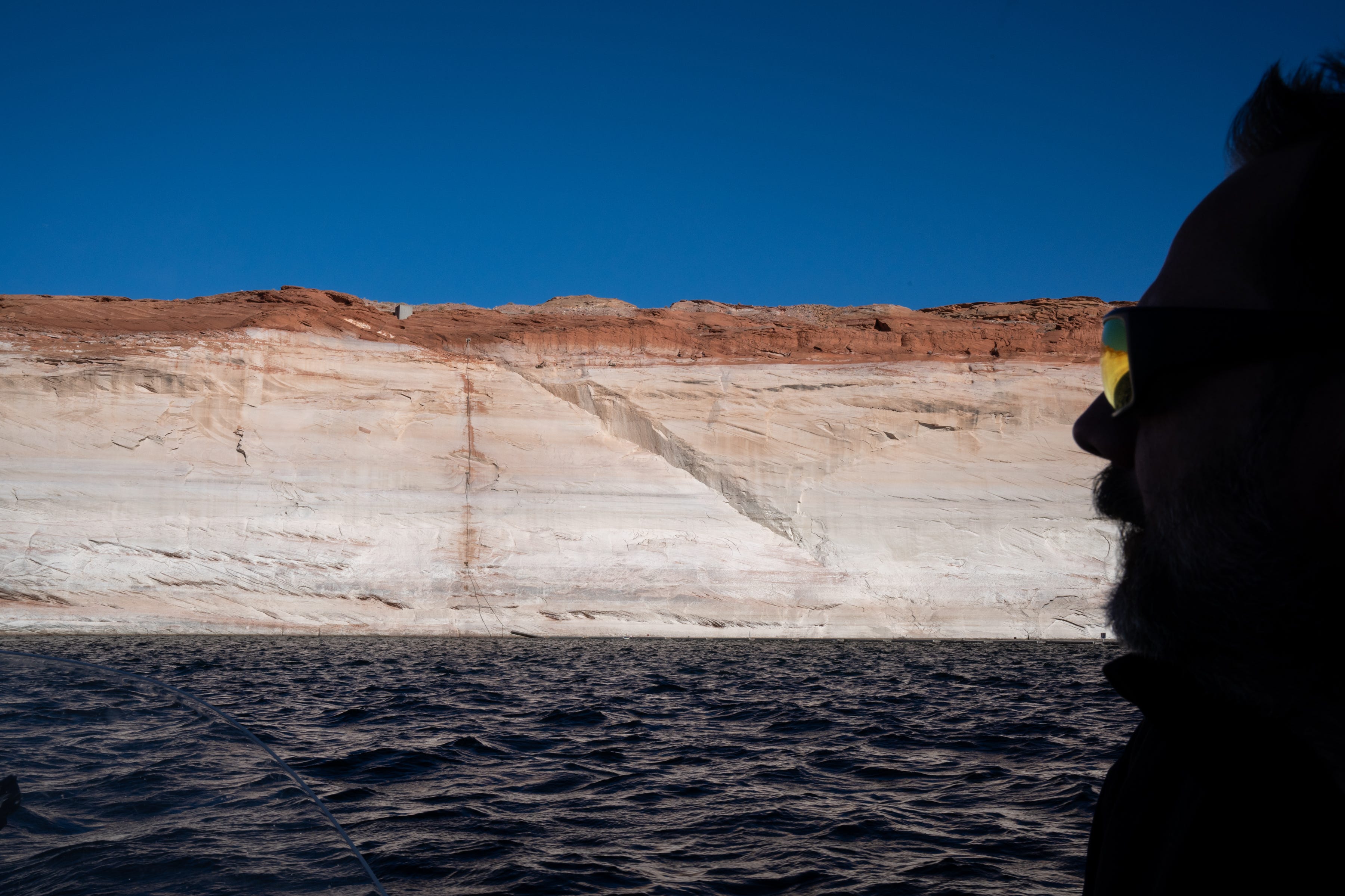 Guide Paul McNabb fishes for striped bass on Feb. 2, 2022, near Glen Canyon Dam near Page. A high-water mark or bathtub ring is visible on the shoreline; Lake Powell was down over 168 vertical feet, at the time.