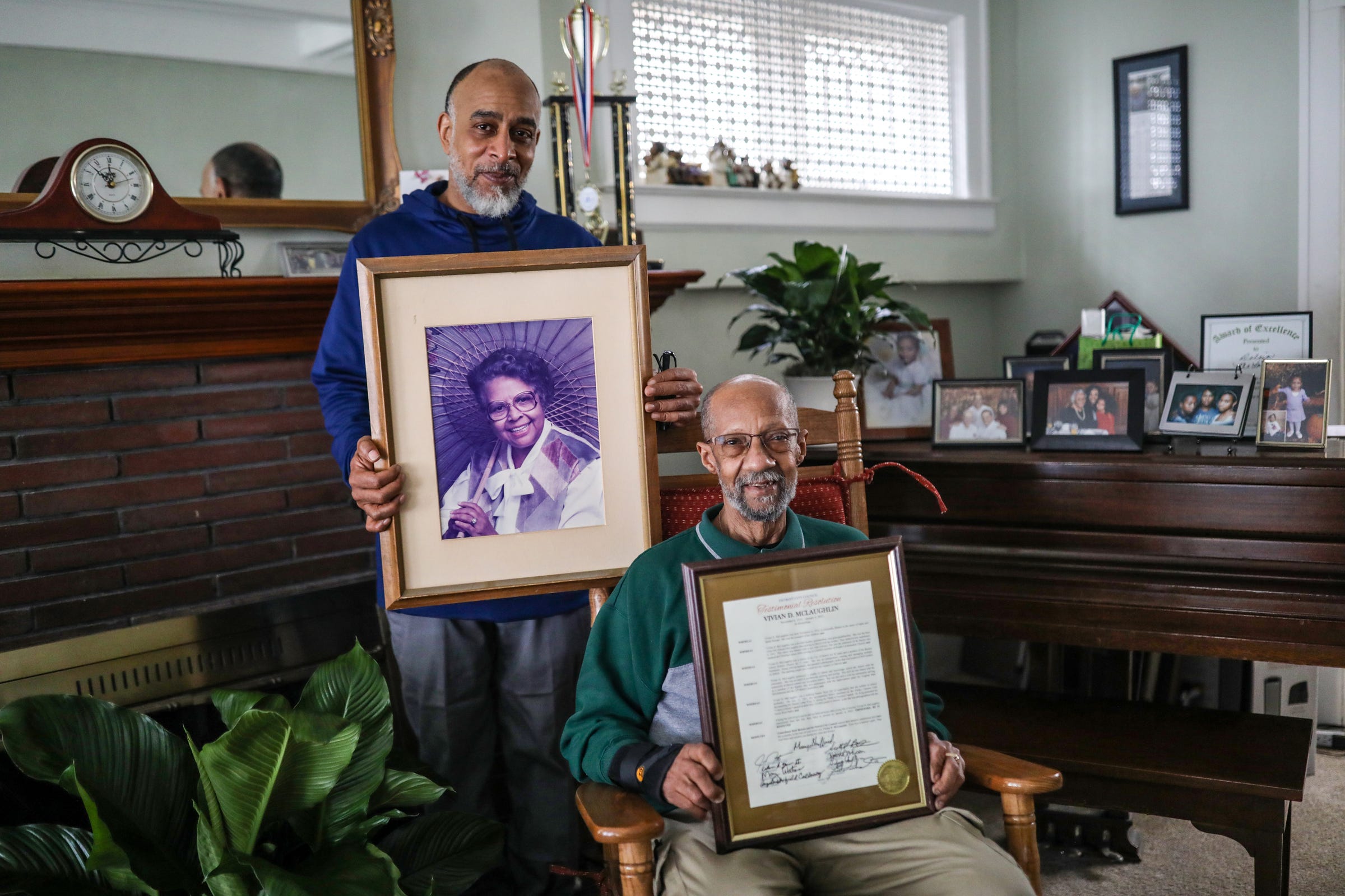 Adrian Ponder, 73, of Royal Oak, right, holds up Detroit City Council proclamation for his late Aunt Vivan McLaughlin,  sitting in her rocking chair next to her grandson Jonathan McLaughlin, who took care of her for 15 years, at her home in Detroit on Tuesday, Feb. 8, 2022. Ponder retired from the Detroit Police Department in 1986 after witnessing his partner being shot and killed on duty. Suffering from Post Traumatic Stress Disorder, Ponder's relationship through the years with McLaughlin has helped him to heal to the point where he can perform his security job today at Wayne State University.