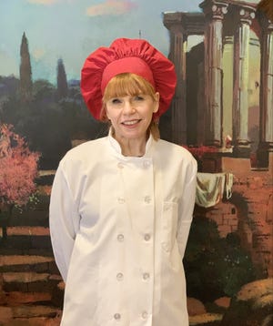 Tonya Garrido, the chef, poses in front of a mural in the formal dining room at Harwood Place Retirement Community. The dining room is a Tuscan theme.