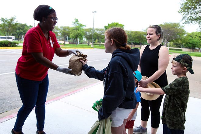 In this April, 2020 file photo, Tiffany Owens, marketing manager for the Round Rock school district food services department, hands meals to students Lola, Bodie and Wyatt, who are accompanied by their mother, Lacy Grace. [PHOTO BY ARIANA GARCIA]