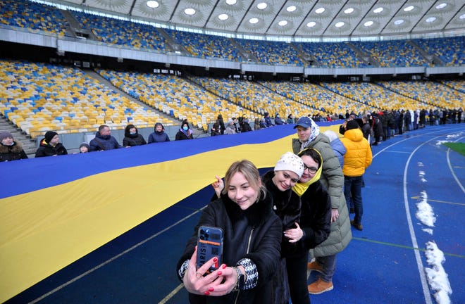 People take pictures as they carry a giant Ukraine's national flag at a stadium to mark a "Day of Unity" in Kyiv on Feb. 16, 2022. Ukrainian leaders urged a "Day of Unity" to rally patriotic support and defy fears of a Russian invasion, as Moscow announced an end to military drills in occupied Crimea.