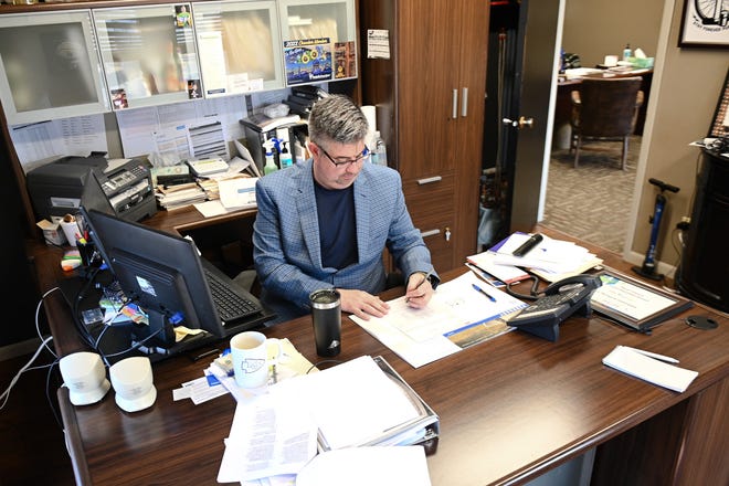 Dave Inskeep, owner of Joe McGuire Insurance, reviews papers spread across his desk as he boots up his computer to begin the workday.