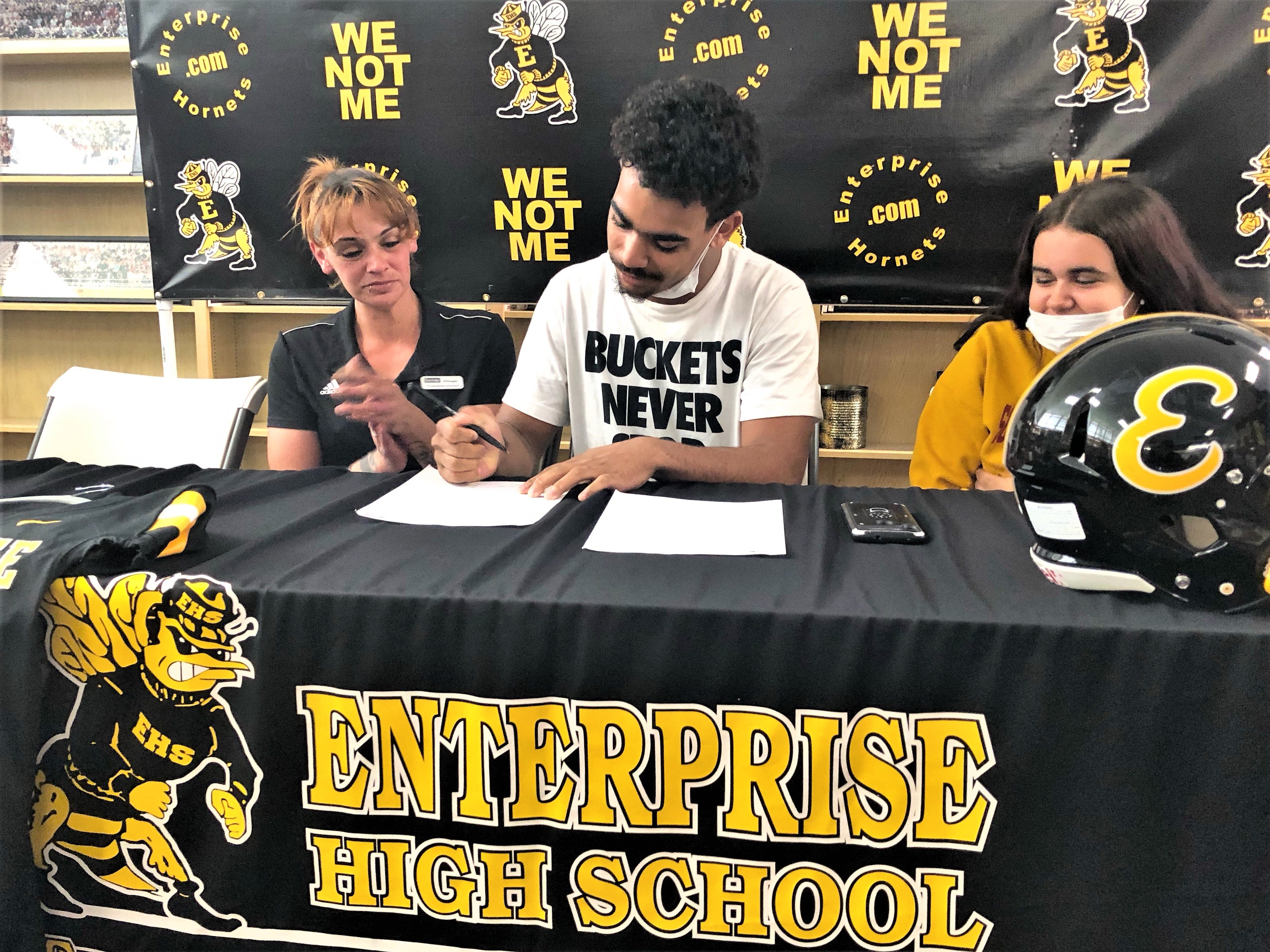 Enterprise High School football player O'Sirus Peoples signs a letter of intent on Feb. 3, 2022, to play football at Southern Oregon University in Ashland, Oregon, in the school's library while seated next to his mother, Melissa Henry, left, and sister Sarah Mitchell.