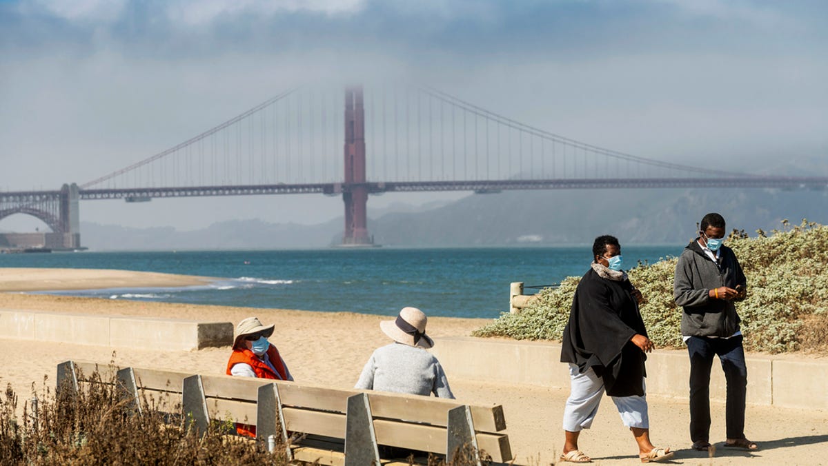 With the Golden Gate Bridge in the background, people wear face masks while strolling at Crissy Field East Beach in San Francisco.