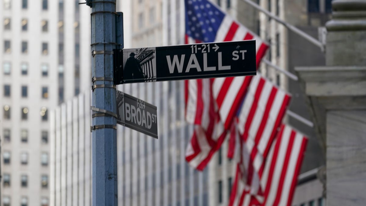 The Wall St. street sign is framed by the American flags flying outside the New York Stock exchange