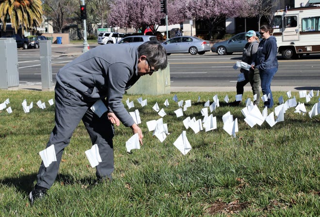 The Rev. Heather Hennessey of Pilgrim Congregational Church, left, inserts small flags into the lawn outside Redding (Calif.) City Hall on Tuesday, Feb. 22, 2022, as a memorial to the 545 Shasta County residents who have died from COVID-19.