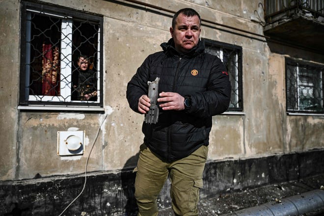 A man holds the remains of a mortar which exploded in front of a building in the town of Schastia, near the eastern Ukraine city of Luhansk, on Feb. 22, 2022, a day after Russia recognized east Ukraine's separatist republics and ordered the Russian army to send troops there as "peacekeepers."