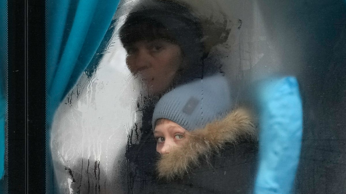 A woman and child peer out of the window of a bus as they leave Sievierodonetsk, the Luhansk region, eastern Ukraine, Thursday, Feb. 24, 2022. Russian President Vladimir Putin on Thursday announced a military operation in Ukraine and warned other countries that any attempt to interfere with the Russian action would lead to "consequences you have never seen."