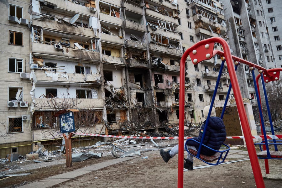 A child on a swing outside a residential building damaged by a missile on February 25, 2022 in Kyiv, Ukraine. Russia began a large-scale attack on Ukraine, with Russian troops invading the country from the north, east and south, accompanied by air strikes and shelling.