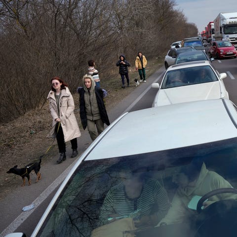 Ukrainian refugees walk along vehicles lining-up t