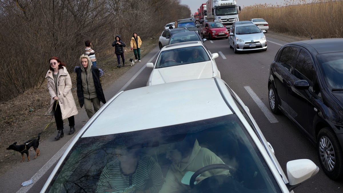 Ukrainian refugees walk along vehicles lining-up to cross the border from Ukraine into Moldova, at Mayaky-Udobne crossing border point near Udobne, Ukraine, Saturday, Feb. 26, 2022.