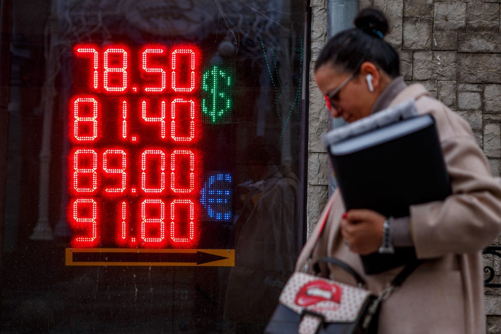 A woman walks past a board showing currency exchange rates of the US dollar and the euro against Russian ruble in Moscow on Feb. 22, 2022. Global sanctions have hit Russia's financial markets and individuals.