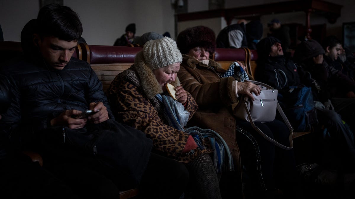 A Ukrainian elderly woman eats a slice of bread inside a crowded Lviv railway station, Monday, Feb. 28, 2022, in Lviv, west Ukraine. Russia's military assault on Ukraine has entered its fifth day, forcing hundreds of thousands of Ukrainians and foreign residents to escape from war and seek refuge in neighboring countries.