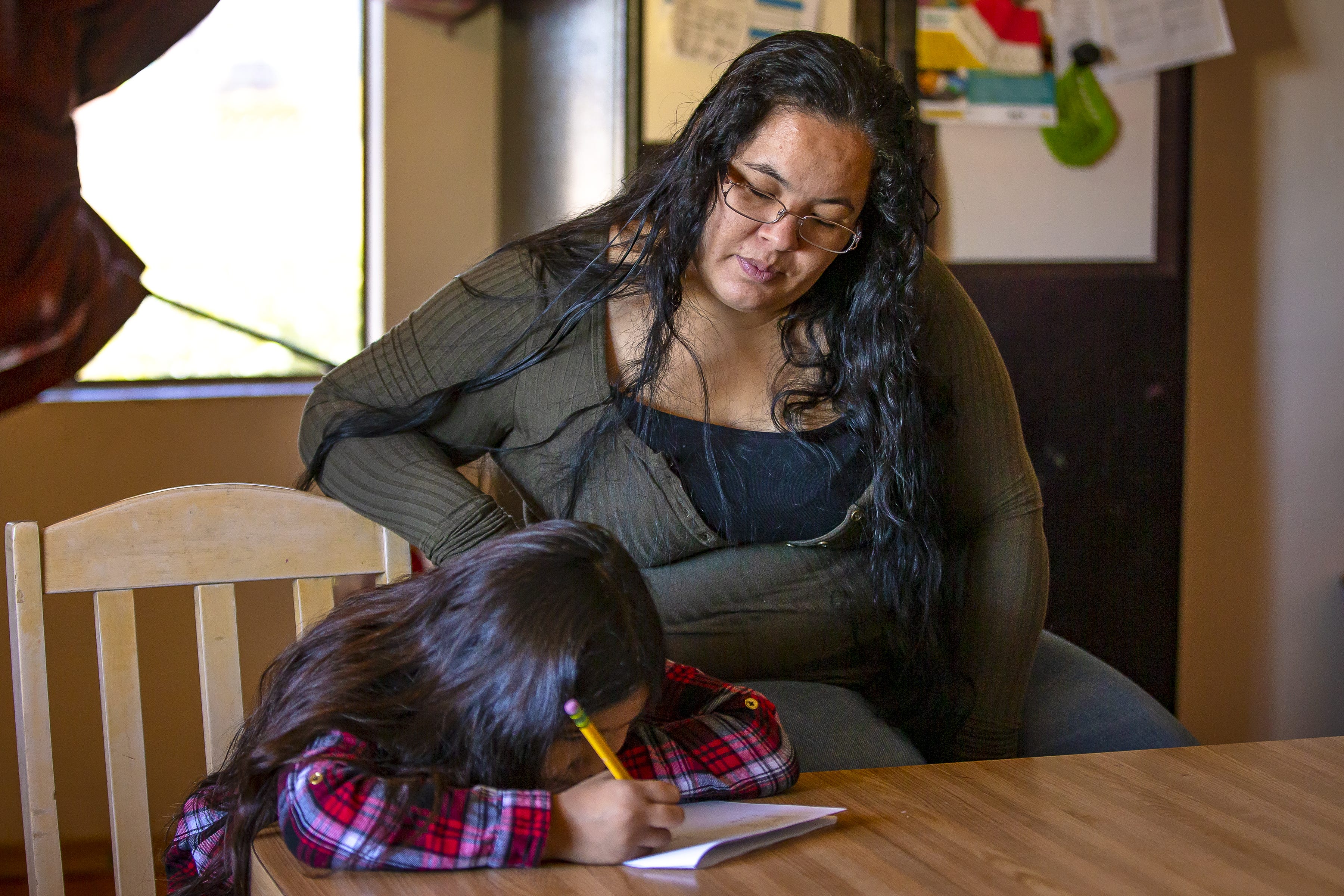 Fernanda Davila, 8, works on homework as her mother, Anarely Jimenez, looks over her progress in their Phoenix home on March 8, 2022.