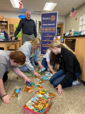 Mel Honig, a Sylvania Rotary member and Interact coordinator, watches as Wynford Interact (Rotary Youth) members, from left, Connor Bloomfield, Aleece Filliater, Elyssa Roberts and Cassandra Kurek apply teamwork to solve a puzzle. The local club presented a check to Honig for mission work in education.