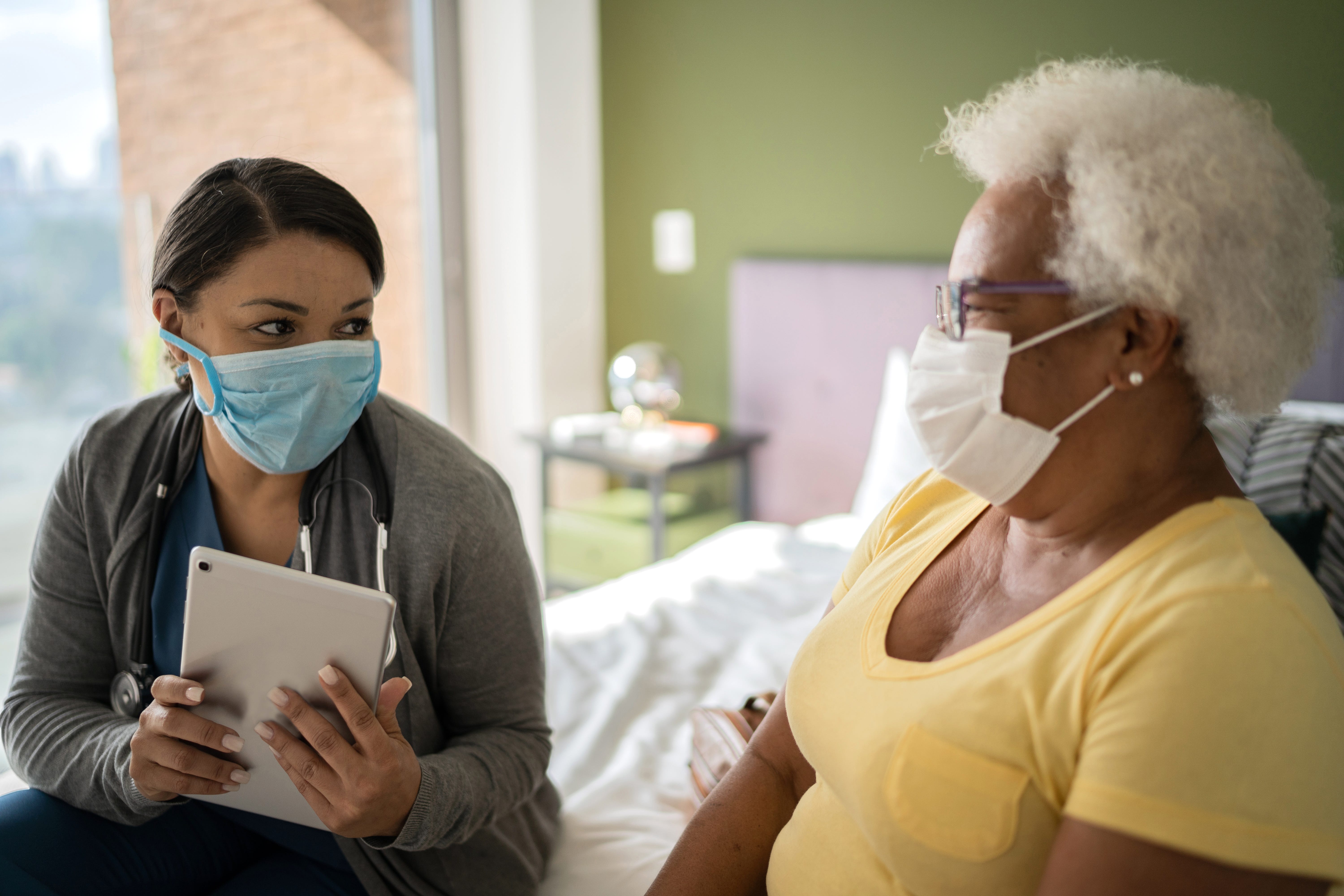 Doctor talking to patient during home visit - wearing protective face mask