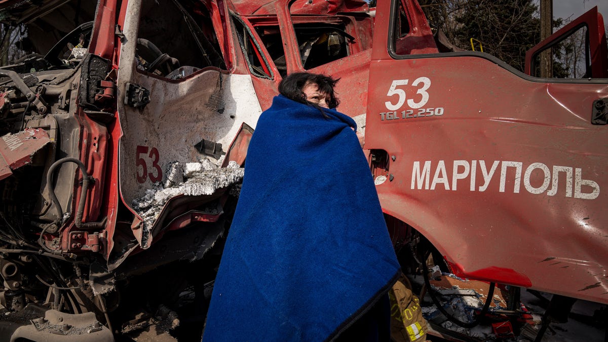 A woman covers herself with a blanket near a damaged fire truck after shelling in Mariupol, Ukraine, Thursday, March 10.