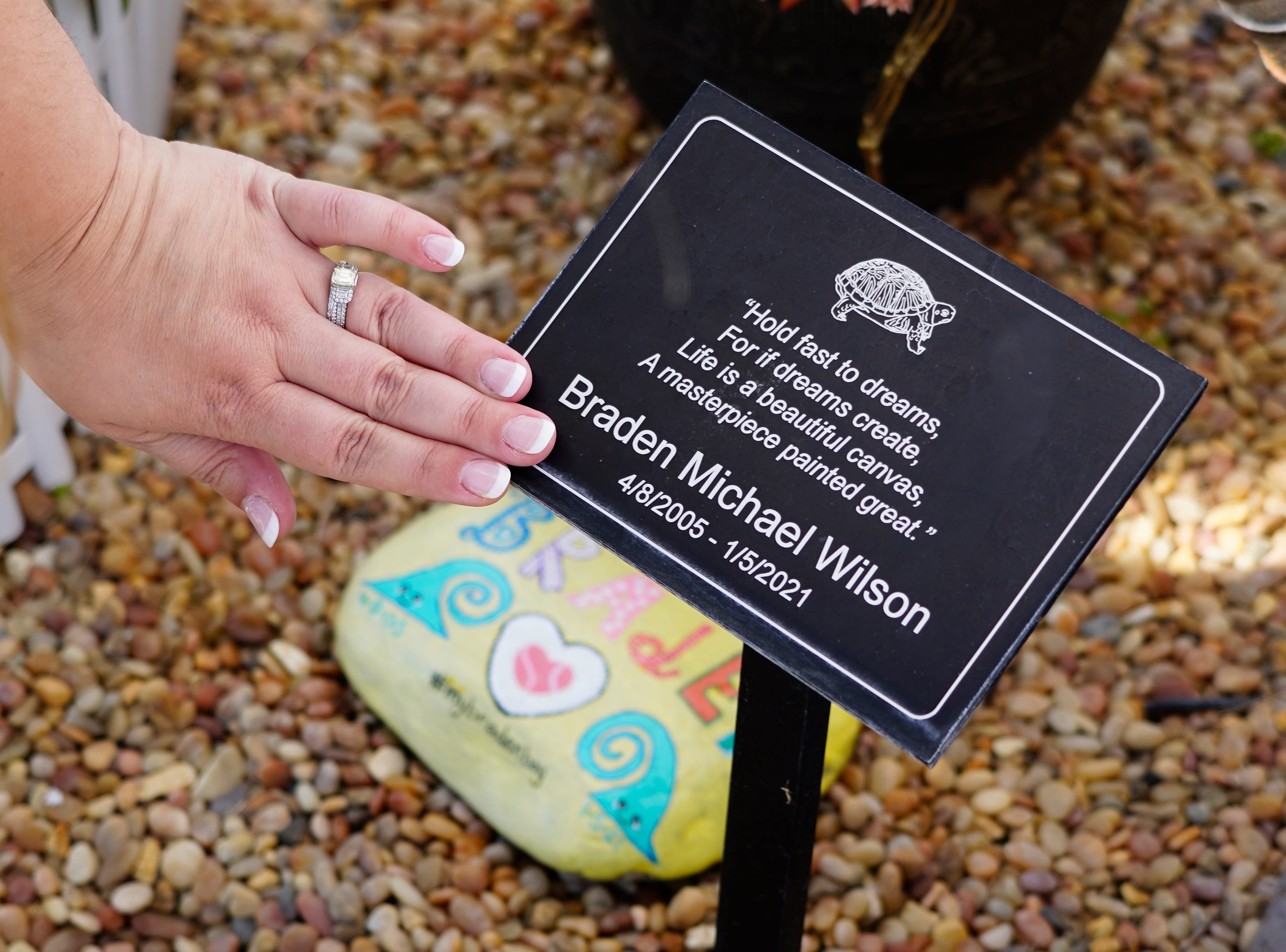 Amanda Wilson wipes off dust on a sign at a free library at her home in Simi Valley, Calif. in March, 2022. The sign is a quote from her 15-year-old son, Braden who died in January 2021 after contracting COVID-19 in December 2020.