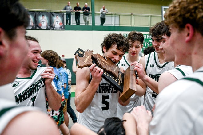 Williamston's Jackson Newman, center, bites the championship trophy after beating Lansing Catholic in the Division 2 regional final on Wednesday, March 16, 2022, at Williamston High School.