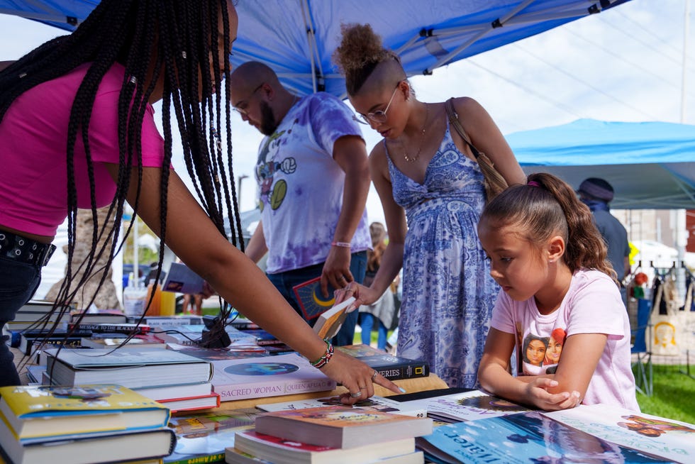 Jocelyn Masese, front left, points to a book for Gisella Anderson, front right, at the Grassrootz Bookstore booth at the Buy Black Marketplace hosted by Archwood Exchange on Roosevelt Row in Phoenix on March 19, 2022.