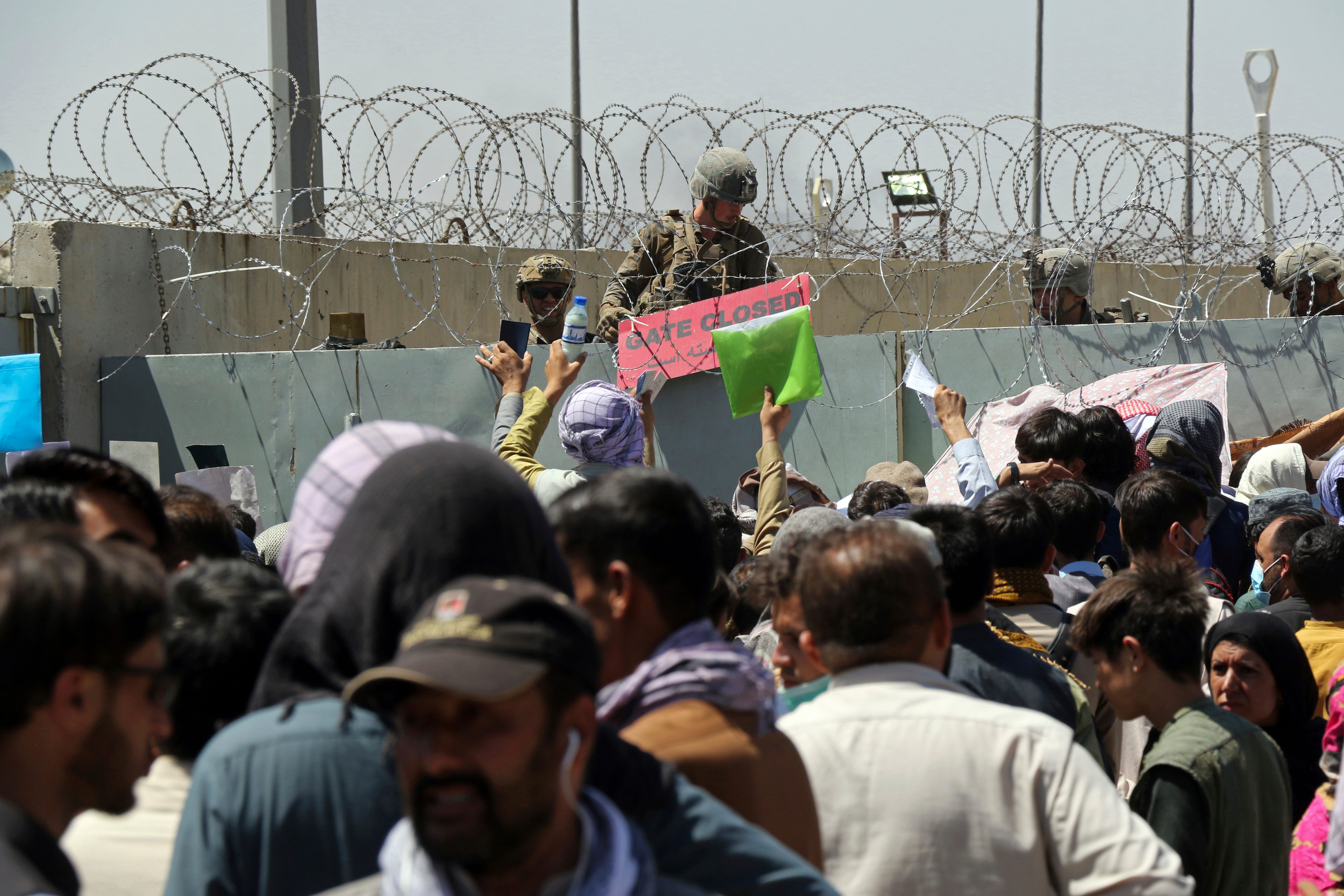 A U.S. soldier holds a sign indicating a gate is closed as hundreds of people gather some holding documents, near an evacuation control checkpoint on the perimeter of the Hamid Karzai International Airport, in Kabul, Afghanistan, Thursday, Aug. 26, 2021. Western nations warned Thursday of a possible attack on Kabul’s airport, where thousands have flocked as they try to flee Taliban-controlled Afghanistan in the waning days of a massive airlift. Britain said an attack could come within hours. 